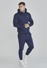Navy blue hoodie and joggers made from a smooth, stretchy fabric. Features a front pocket, ribbed cuffs, and a small logo on the chest.