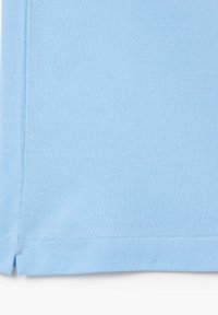 Ljusblått, strukturerat tyg med ett vävt mönster. Sömmen har en liten slits på varje sida för enklare rörelse. Standard passform.