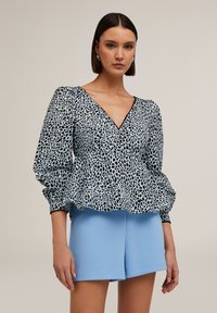 Top peplum color azzurro chiaro con motivo a macchie nere, con scollatura a V profonda e maniche a sbuffo. Abbinato a pantaloni corti solidi azzurro chiaro.