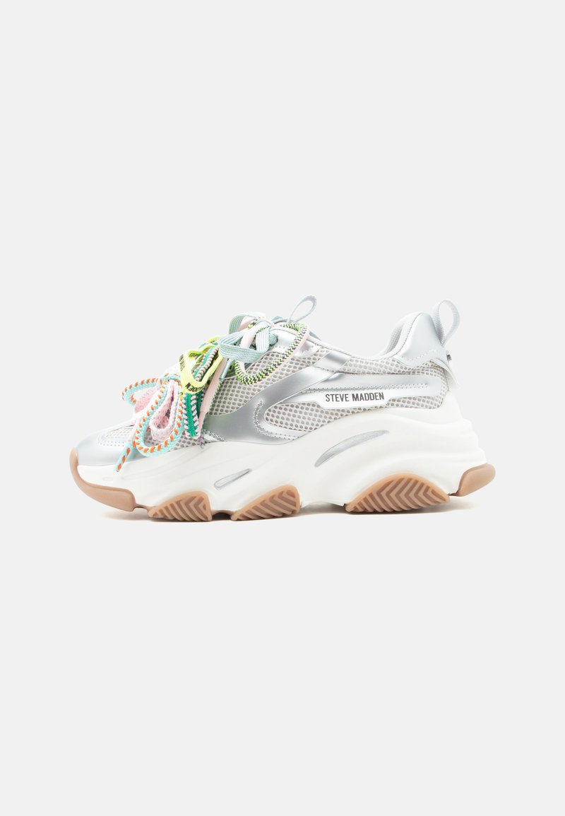 Χοντρό λευκό αθλητικό παπούτσι με ασημί πλέγμα στις πλευρές, πολύχρωμα κορδόνια, μπεζ λαστιχένια σόλα και το λογότυπο "Steve Madden" στο πλάι.