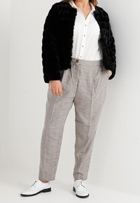 Sort jakke i kunstpels, hvid skjorte med knapper og højtaljede ternede bukser. Hvide brogues fuldender outfittet med et tekstureret udseende.