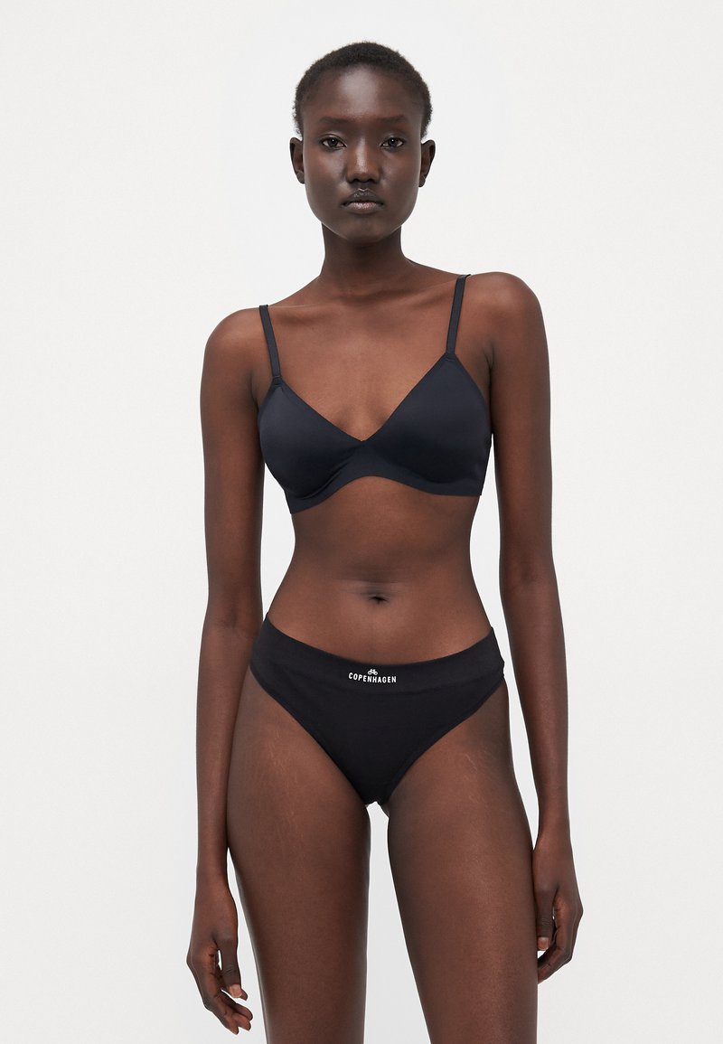 Black bra and bikini set made of smooth stretch fabric. The bra features thin straps and a v-shaped design, while the bikini has a wide waistband with “Copenhagen” text.