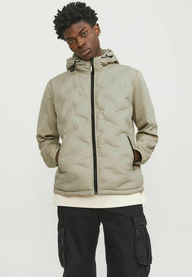 Gevoerde zip-up jas in licht olijfgroen, met een capuchon, zwarte rits en zijzakken. Het materiaal lijkt glad met zichtbare stiksels.