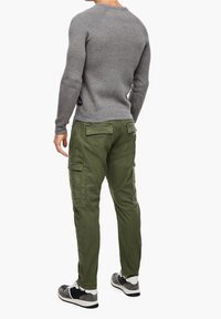 Pull en maille gris, pantalon cargo vert avec plusieurs poches, et baskets noires et grises sportives. Tissu texturé et design ajusté.