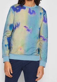 Felpa multicolore con una base blu e motivi astratti in verde, viola e giallo. Maniche e orlo a coste in blu chiaro.