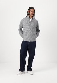 Grå og hvit rutete skjorte med knapper og lange ermer, kombinert med mørkeblå vide jeans og hvite treningssko.