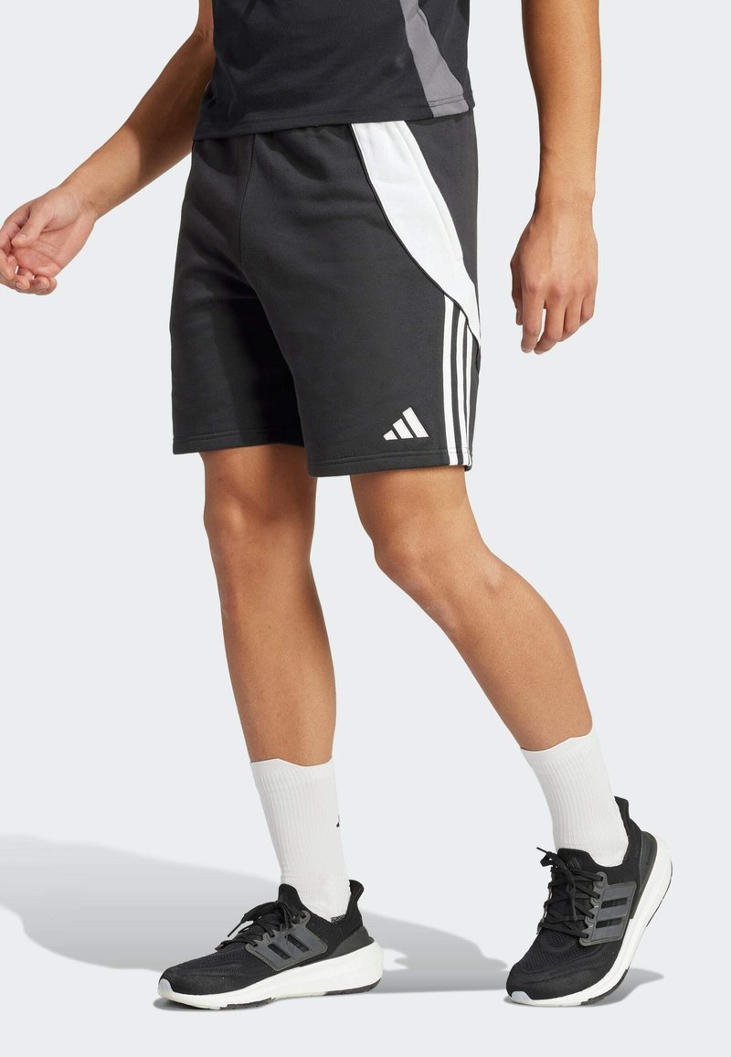 Shorts de sport noirs avec panneaux latéraux blancs et trois bandes verticales, fabriqués dans un matériau doux. Portés avec des chaussures noires et des chaussettes blanches.
