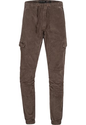 Bruna cargo-byxor med elastisk midja, sidofickor, avsmalnande ben och en texturerad bomullstyg. Har justerbara muddar vid anklarna.