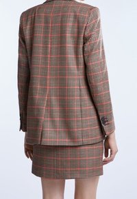 Blazer a quadri marrone con accenti rossi, caratterizzato da un design aderente, uno spacchetto posteriore e una gonna mini coordinata a quadri. Tessuto testurizzato con dettagli in bottoni.