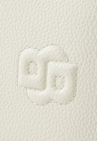 Textured white leather surface featuring an embossed logo with rounded edges and small cut-out details, highlighted by contrasting stitching.