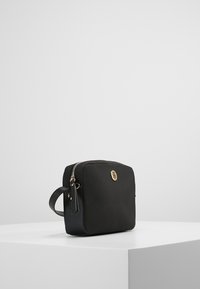 Borsa rettangolare nera realizzata in materiale opaco con una zip dorata, manico laterale e logo embossato sulla parte frontale. Pannello laterale testurizzato.