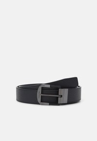 Cintura in pelle nera con superficie testurizzata, dotata di una fibbia in metallo argentato e un'etichetta con la scritta "Calvin Klein" incisa. Bordi lisci.