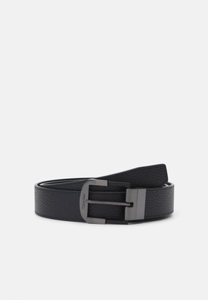 Cintura in pelle nera con superficie testurizzata, dotata di una fibbia in metallo argentato e un'etichetta con la scritta "Calvin Klein" incisa. Bordi lisci.