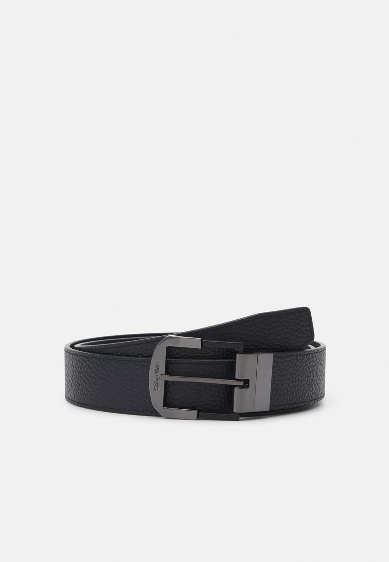 Cintura in pelle nera con superficie testurizzata, dotata di una fibbia in metallo argentato e un'etichetta con la scritta "Calvin Klein" incisa. Bordi lisci.