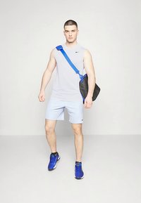Débardeur de sport gris, short bleu clair et baskets bleues. Sac à épaule noir avec une sangle bleue. Style simple et sportif.