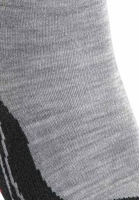 Grå sok med en tæt strikket tekstur, med en sort sektion og tynde hvide striber. Materialet synes elastisk og holdbart.