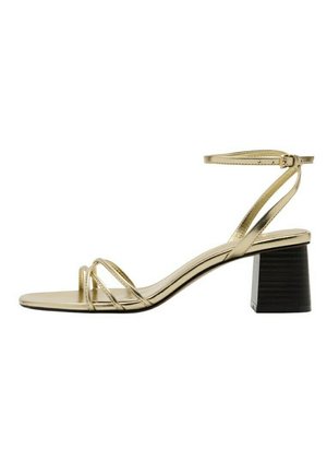 Sandalia dorada con tiras y correa ajustable en el tobillo, tacón cuadrado en negro, con delgadas tiras delanteras y diseño de punta abierta.