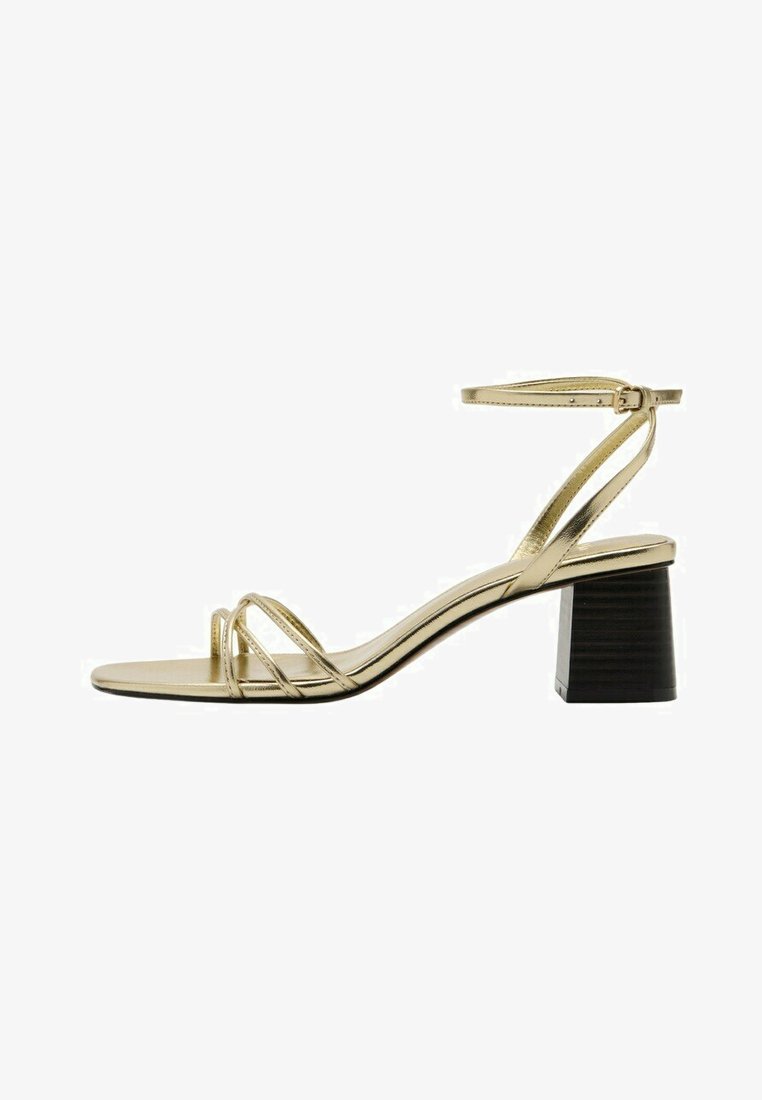 Sandale dorée à brides avec bride de cheville ajustable et talon bloc noir, présentant de fines lanières à l'avant et un design à bout ouvert.
