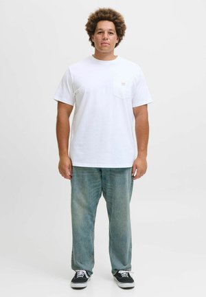 Camiseta de algodón blanca de manga corta con un bolsillo en el pecho, combinada con vaqueros claros de corte holgado y zapatillas negras.