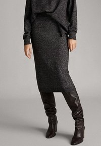 Grauer Strickrock mit geradem Schnitt, der bis zur Mitte der Wade reicht, kombiniert mit kniehohen braunen Lederstiefeln, die Textur und Glanz zeigen.