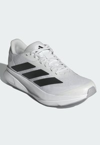 Weißer Sportschuh mit einem Obermaterial aus Mesh, schwarzem Drei-Streifen-Design, runder Zehenform, strukturiertem Sohle und Schnürverschluss.