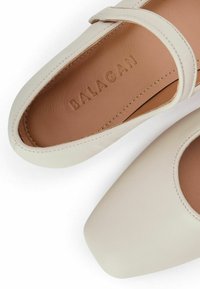 Zapatos de cuero crema con punta cuadrada y una tira delgada a través del empeine, con una textura suave y un interior beige embellecido con "BALAGAN."