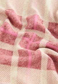 Mīksts austa audums rozā un bēšā krāsā, ar pārbaudes rakstu, kas ietver teksturētas kvadrātus un plānas svītru akcentus. Ērts un viegls.