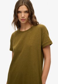 Oliwkowy t-shirt wykonany z miękkiej bawełny, z okrągłym dekoltem i podwiniętymi krótkimi rękawami, o luźnym kroju i gładkiej fakturze.