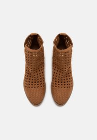 Botas de tobillo trenzadas marrones con diseño perforado y lazos en la parte trasera, mostradas desde una vista superior sobre un fondo blanco.