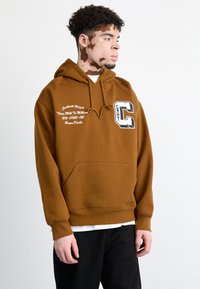 Sudadera marrón con capucha, con un bolsillo tipo canguro, texto blanco y una gran gráfica de "C" en la parte frontal. Puños y dobladillo acanalados.