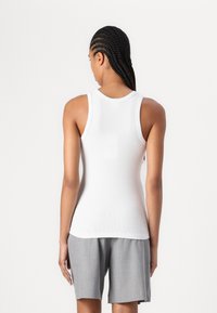Weißes, geripptes Tanktop mit rundem Ausschnitt. Trägt es mit hellgrauen Shorts, die eine lockere Passform und ein gefaltetes Design aufweisen. Rückansicht dargestellt.