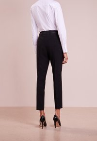 Pantalons noirs ajustés avec une coupe slim, en tissu lisse, au design simple, avec une taille mi-haute, associés à des talons noirs pointus.