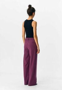 Lilla vide bukser med elastisk talje og to baglommer, parret med en tætsiddende sort tanktop, set fra ryggen.