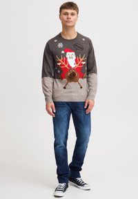 Grauer Weihnachtspullover mit einem Design von Santa und einem Rentier, gestrickte Textur, mit Schneeflocken und Akzenten in Rot und Braun. Blaue Jeans und Turnschuhe.