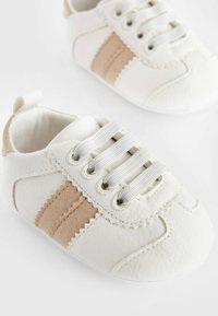 Zapatitos de bebé blancos hechos de cuero con una textura suave. Presentan rayas de ante beige, cordones elásticos y un diseño de punta redonda.