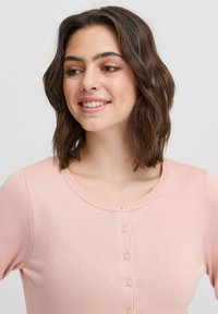 Cardigan lavorato a maglia di colore rosa chiaro con scollatura a barca, dotato di chiusura con bottoni lungo la parte anteriore e una sottile texture a costine.