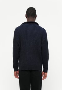 Ciemnoniebieski sweter prążkowany z szerokim kołnierzem, długimi rękawami i luźnym krojem. Materiał wydaje się miękki i ma teksturowaną powierzchnię.