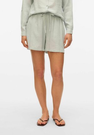 Hellgrüne Leinenshorts mit elastischem Bund und Kordelzug, entspannter Passform und gesäumten Kanten. Getragen mit braunen Flip-Flops.