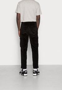 Černé kordové cargo kalhoty s bočními kapsami, v kombinaci se šedým tričkem a černými teniskami. Hladká textura, štíhlý střih.