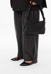 Černá kožená kabelka s ozdobným páskem, oválným tvarem a raženým logem. Kombinována s černými širokými lesklými kalhotami a špičatými balerínami.