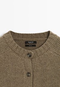 Cardigan en laine tricotée marron avec col côtelé et deux boutons foncés sur le devant, affichant l'étiquette de la marque à l'intérieur du col.