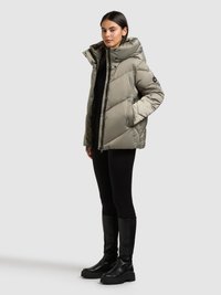 Polsterēta olīvu zaļa jaka ar augstu apkakli, rāvējslēdzēja aizdari un lielām kabatām. Valkāta ar melnām legingām un melniem zābakiem līdz ceļiem.