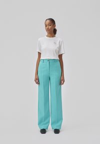 T-shirt en coton blanc à manches courtes avec un petit graphique sur la poitrine gauche, associé à un pantalon taille haute à jambes larges en turquoise.