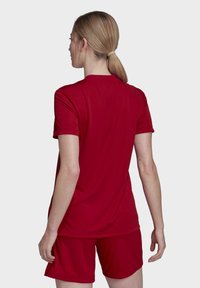 Rotes Sport-T-Shirt mit glatter Textur und kurzen Ärmeln, kombiniert mit passenden roten Shorts, von hinten vor einem neutralen Hintergrund gezeigt.