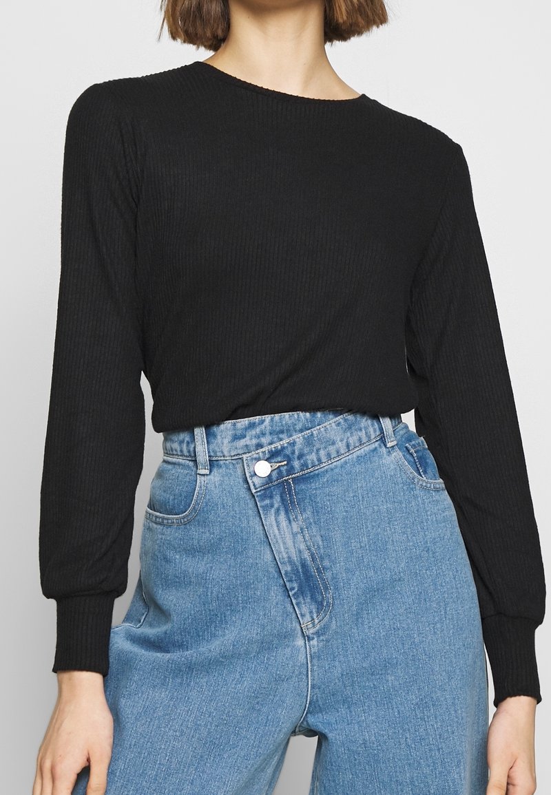 Maglietta nera a maniche lunghe con motivo a coste e collo tondo, abbinata a jeans in denim azzurri a vita alta con dettagli di bottoni e tasche.