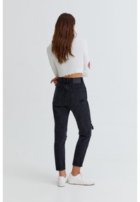 Black high-waisted jeans with distressed detailing and a tapered leg, paired with a white cropped top featuring a scalloped hem.
