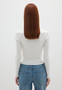 Ripp weißes Langarmshirt, kombiniert mit hochtaillierten blauen Jeans, die eine taillierte Silhouette und eine weiche Textur aufweisen.