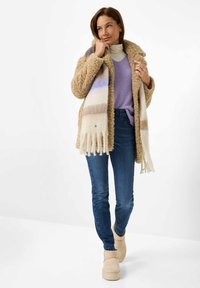 Lysbrun fluffy frakke, lilla strikket sweater, blå jeans og beige støvler. Et stribet tørklæde i creme, lavendel og taupe fuldender outfittet.