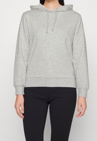 Grijze hoodie van zacht materiaal met een trekkoordcapuchon, lange mouwen en een ribbelrand. Gecombineerd met zwarte broek. Eenvoudig ontwerp.