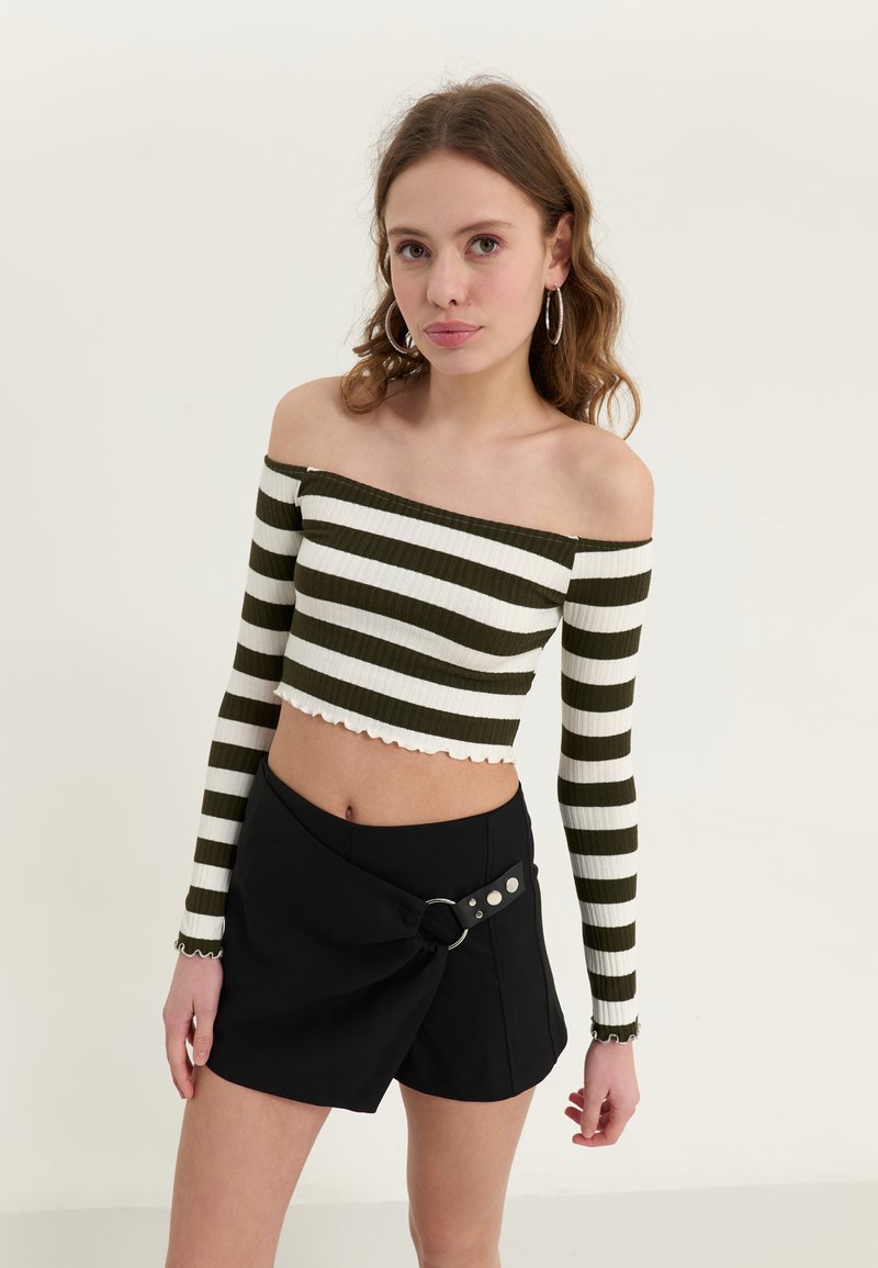 Lyhyempi off-the-shoulder-toppu ribbikankaasta, jossa on vihreitä ja valkoisia vaakaraitoja. Yhdistetty mustaan rypytettyyn hameeseen, jossa on soljetyylinen yksityiskohta.